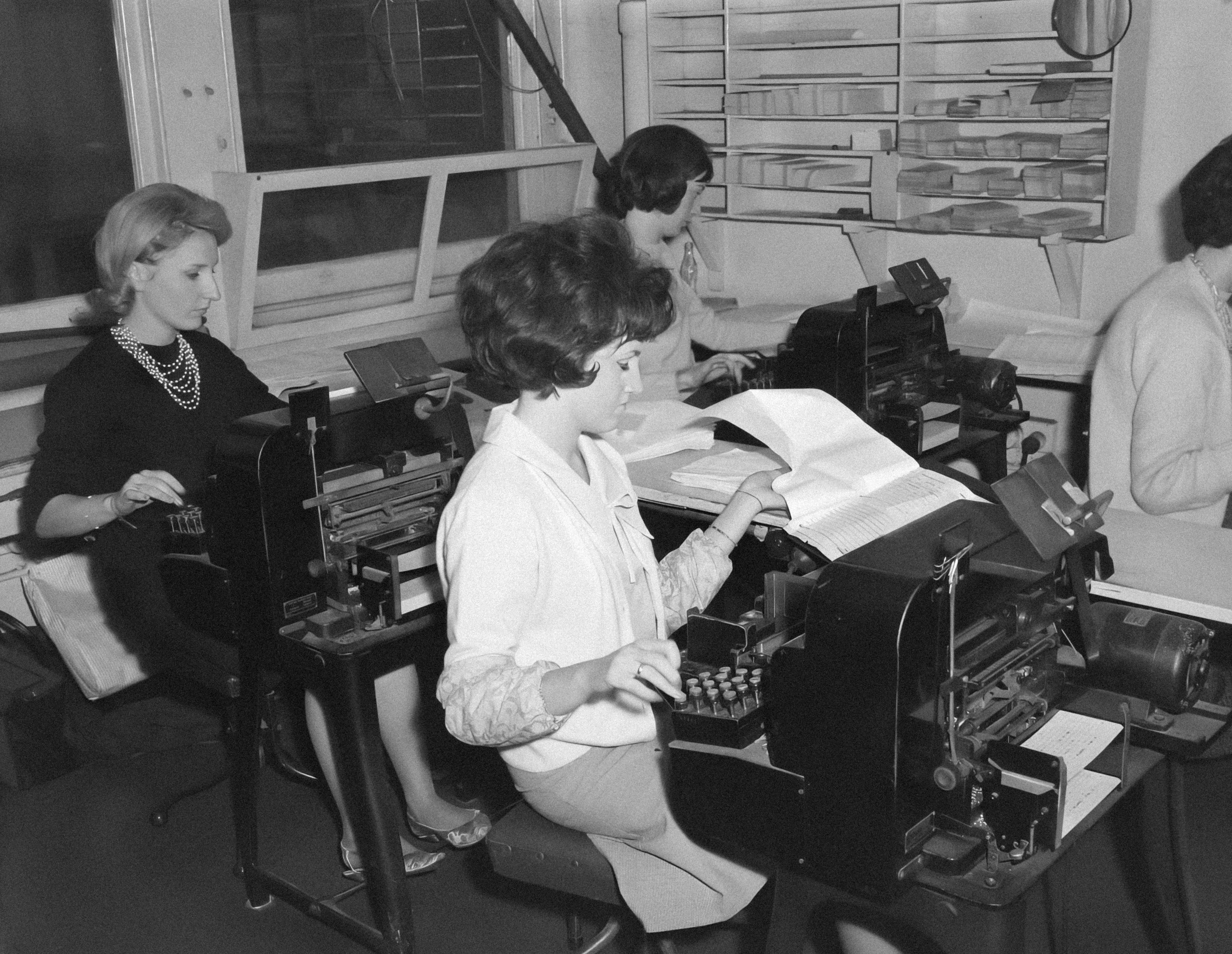 a group of women sitting at a table working on a typewriter